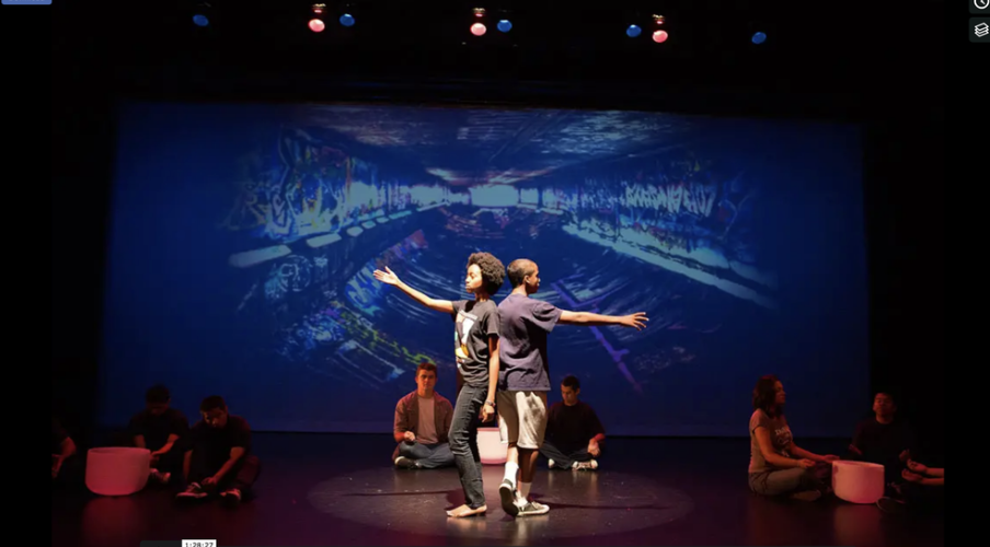 Two performers on stage in front of a projected backdrop