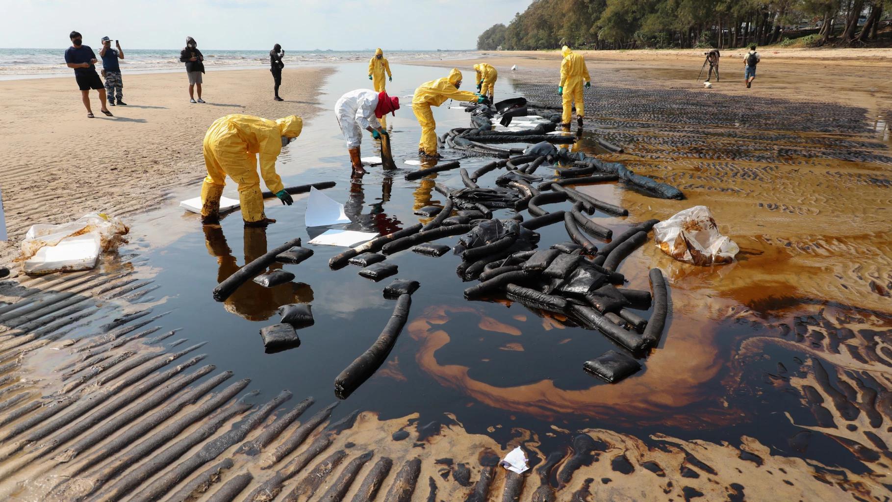 Workers in yellow protective suits containing an oil spill on a beach