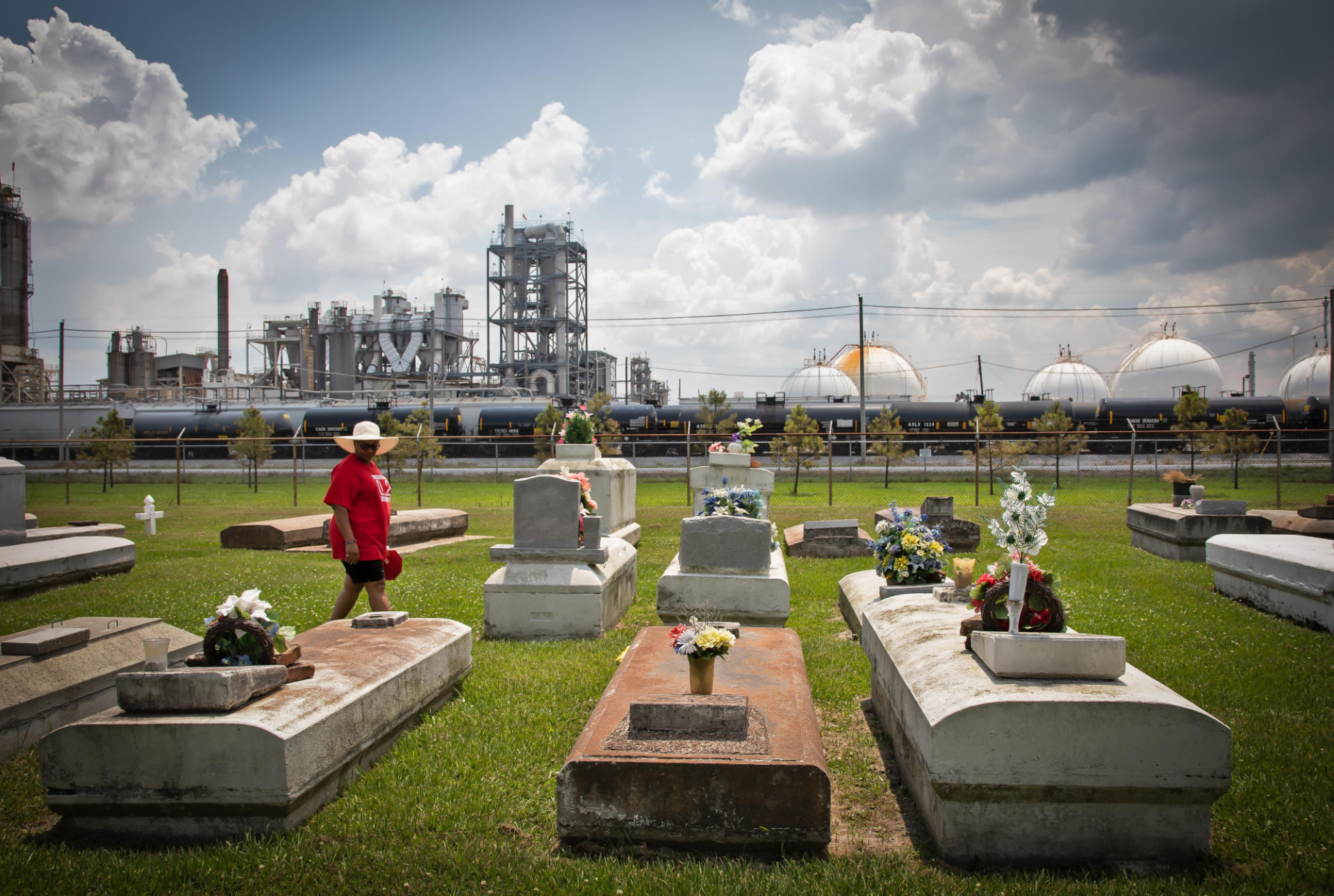 Woman walking through a cemetery beside a petrochemical plant in Cancer Alley